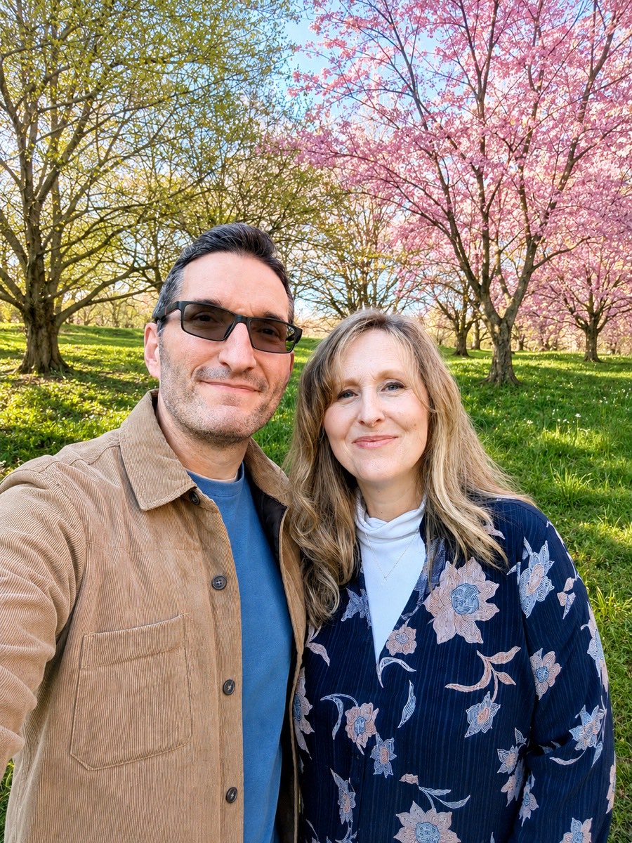 Nathan and Emily Sanders standing together outdoors under blossoming trees in daylight.