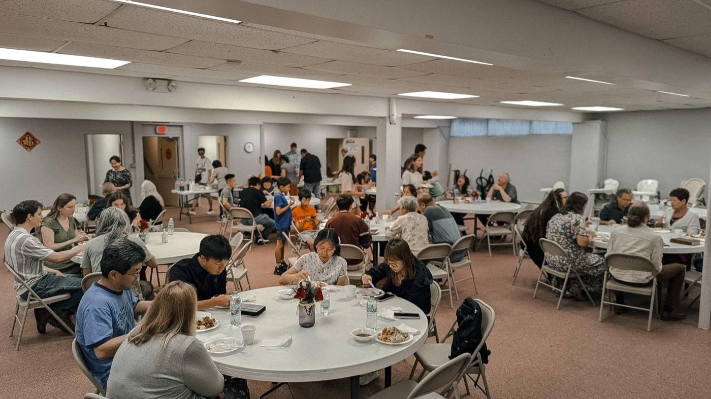 People eating and talking around round tables in a hall after a gathering.